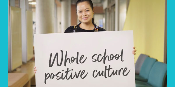Photo of a woman holding up a board with writing 'Whole school positive culture'.